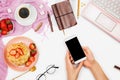 Beautiful flatlay arrangement with cup of coffee, hot waffles with cream and strawberries, laptop and woman hand`s holding smartp