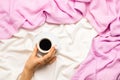 Beautiful flatlay with woman`s hand holding a cup of morning coffee in bed