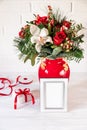 Beautiful flower arrangement of white orchid, red roses, natural spruce branches in red vase with photo frame infront, gift box on Royalty Free Stock Photo