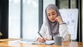 A focused Asian Muslim businesswoman is signing documents, or taking notes on paper at her desk Royalty Free Stock Photo