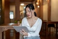 A beautiful and focused Asian woman is using her digital tablet while sitting in a coffee shop Royalty Free Stock Photo