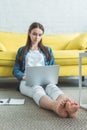 beautiful focused barefoot girl using laptop while sitting on carpet