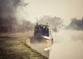 Beautiful foggy misty canal narrow boat sunrise with smoke from chimney early morning sun mist and fog rising from water Royalty Free Stock Photo