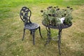 A beautiful forged chair and table stand on a green lawn in the courtyard of the house. There is a flower pot with a Royalty Free Stock Photo