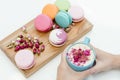 Beautiful french macarons on the desk. Woman hands holding blue cup of cappuccino with roses petals Royalty Free Stock Photo