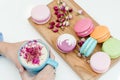 Beautiful french macarons on the desk. Woman hands holding a blue cup of cappuccino with roses petals Royalty Free Stock Photo