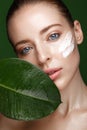 Beautiful fresh girl with cosmetic cream on the face, natural make-up and green leaves. Beauty face.
