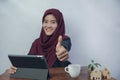 A beautiful, friendly young Muslim business woman smile and thumbs up at camera in hijab dress and suit using laptop