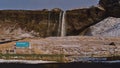 Beautiful front view of famous waterfall Seljalandsfoss in winter with snow-covered meadow and name sign.