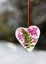 Beautiful frozen heart made of ice, fern leaf and pink hyacinth flowers hanging in a winter snowy garden.