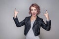 Beautiful funny amazed rocker girl with short hairstyle and makeup in casual style black leather jacket standing with rock sign