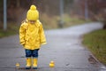 Beautiful funny blonde toddler boy with rubber ducks and colorful umbrella, jumping in puddles and playing in the rain Royalty Free Stock Photo