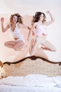 2 beautiful funny girl friends, attractive 2 women having fun amazing jumping high in their pajamas on the bed