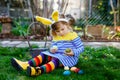 Beautiful funny little toddler girl with bunny ears having fun with traditional Easter eggs hunt on warm sunny day Royalty Free Stock Photo