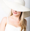 Beautiful funny young blonde woman in white tank top and a large white hat smiling. part of the face covered hat Royalty Free Stock Photo