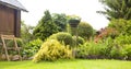 Beautiful garden with blooming flower beds and a wooden garden chair near country house in summer Royalty Free Stock Photo