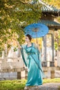 Beautiful geisha with a blue umbrella near green apple tree