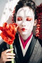 Beautiful geisha holding red flowers in sunlight