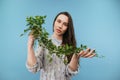 Beautiful gentle lady in a dress posing on a blue background with a flowerpot in her hands, looking at the camera with a serious