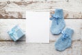 Beautiful gift, baby`s socks and blank postcard on white wooden background. Flat lay