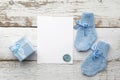 Beautiful gift, baby`s socks and blank postcard on white wooden background. Flat lay