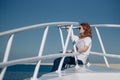 Beautiful ginger woman in sun glasses sits on a white yacht in a sea with clear turquoise water. Relaxation at summer vacation Royalty Free Stock Photo