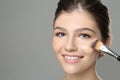 Beautiful girl applying foundation with brush against grey background. Space for text Royalty Free Stock Photo