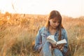 Beautiful girl in autumn field reading a book. The girl sitting on a grass, reading a book. Rest and reading. Outdoor reading Royalty Free Stock Photo