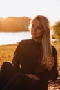 Beautiful girl in autumn landscape at sunset. Autumn portrait of a girl sitting on the grass, selective focus Royalty Free Stock Photo