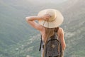 Beautiful girl with a backpack and a wide hat standing with her back against a background of green mountains Royalty Free Stock Photo