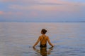 A beautiful girl bathes in the warm sea at sunset. The calm sea reflects the sunset colors of the sky. Royalty Free Stock Photo