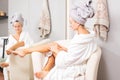 Beautiful girl in bathrobe is applying body lotion her legs. Depilation concept Royalty Free Stock Photo