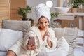 Beautiful girl in bathrobe and with towel on her head making selfie using smartphone on the bed at cozy home. Royalty Free Stock Photo