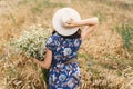 Beautiful girl with big daisies bouquet, back view. Tranquil summer in countryside. Stylish young woman in blue vintage dress and