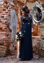 Beautiful girl in a black dress with flowers on the background of an old brick wall with a mirror. Magic black, Gothic beauty, Royalty Free Stock Photo