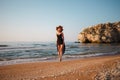 Beautiful girl in a black dress and hat walks along the sea sandy shore at sunset Royalty Free Stock Photo