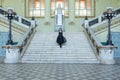 Beautiful girl in black dress running down wide stairs in hall checkered floor