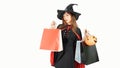 Beautiful girl in black dress and witch hat is holding shopping bags, looking at camera and smiling, on background white. Royalty Free Stock Photo