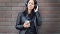 A beautiful girl in a black leather jacket listens to music from external headphones from her phone Royalty Free Stock Photo