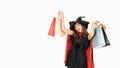 Beautiful girl with black and orange hair in black dress and witch hat is holding shopping bags and smiling on white background Royalty Free Stock Photo