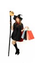 Beautiful girl with black and orange hair in black dress and witch hat is holding staff with shopping bags on white background Royalty Free Stock Photo