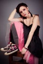 Beautiful girl in black and pink dress and sneakers sitting on a chair cross-legged Royalty Free Stock Photo