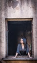 Beautiful girl in black posing in an old window frame. Attractive long hair brunette daydreaming in decaying building. Royalty Free Stock Photo