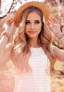 Beautiful girl with blond hair in elegant dress posing among flowering peach trees in garden