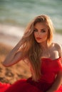 beautiful girl with blond hair in a fluffy red dress sitting along the sea Royalty Free Stock Photo