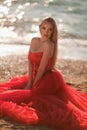 beautiful girl with blond hair in a fluffy red dress sitting and posing along the sea, glamorous stile Royalty Free Stock Photo