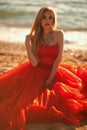 beautiful girl with blond hair in a fluffy red dress sitting and posing along the sea, glamorous stile Royalty Free Stock Photo