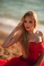 beautiful girl with blond hair in a fluffy red dress sitting and posing along the sea, glamorous stile Royalty Free Stock Photo
