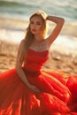 beautiful girl with blond hair in a fluffy red dress sitting and posing along the sea, glamorous stile Royalty Free Stock Photo