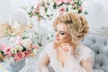 Beautiful girl with blond hair in a peignoir elegantly sits on the couch surrounded by flowers Royalty Free Stock Photo